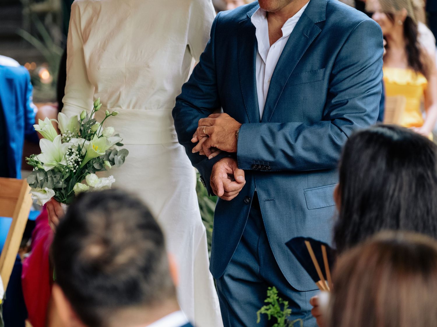 Close-up detail shot of wedding ceremony showing blue suit and white dress with delicate floral bouquet details.
