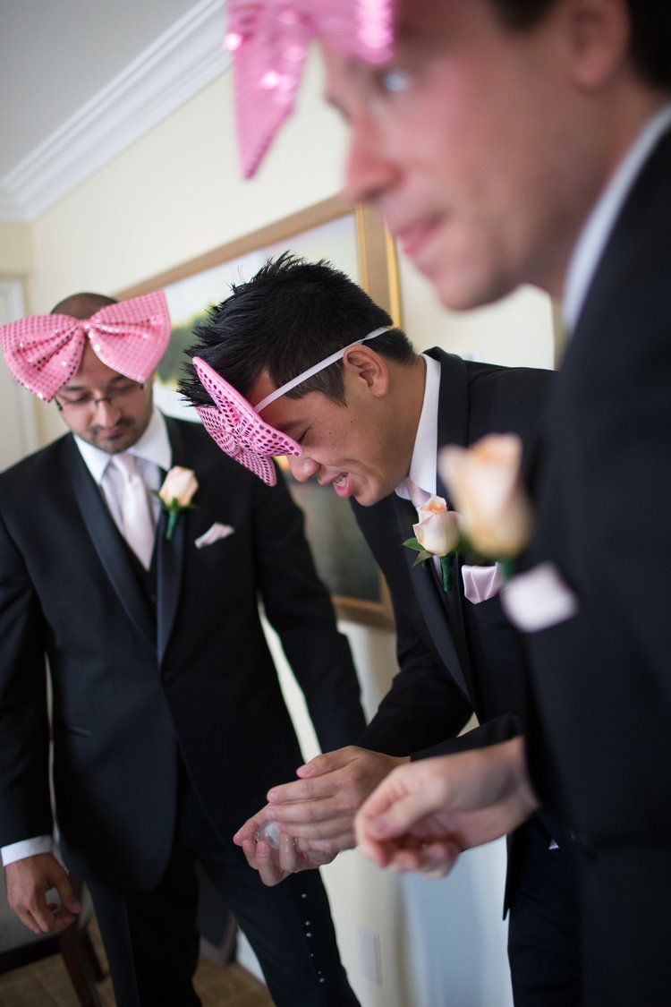 Groomsmen wearing pink bow ties and dark suits share a lighthearted moment before the ceremony.