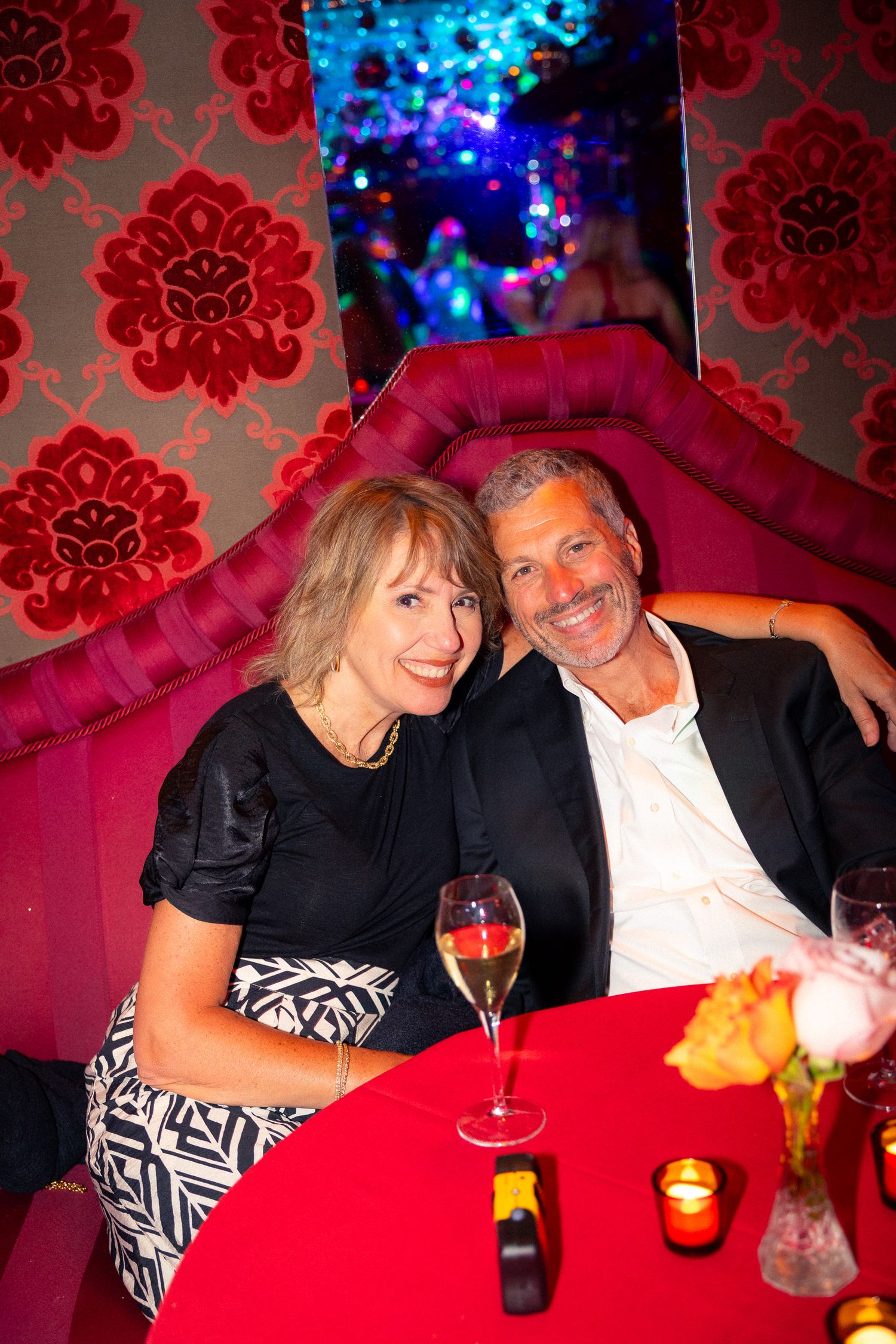 Couple relaxing on red velvet seating with drinks at a lounge bar.