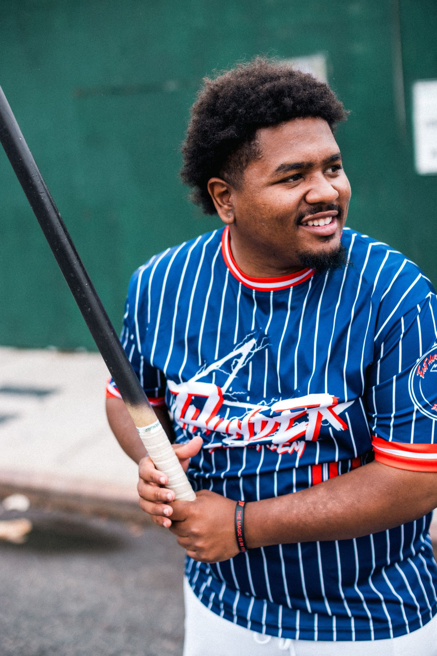 Player wearing striped baseball jersey smiles while holding batting stance during practice.