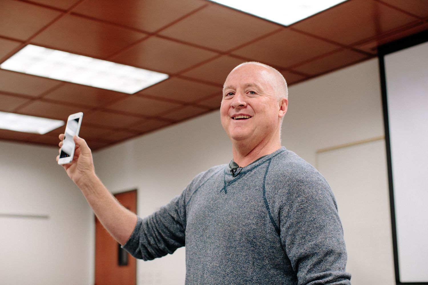 Speaker gesturing while giving presentation in classroom with projector screen.
