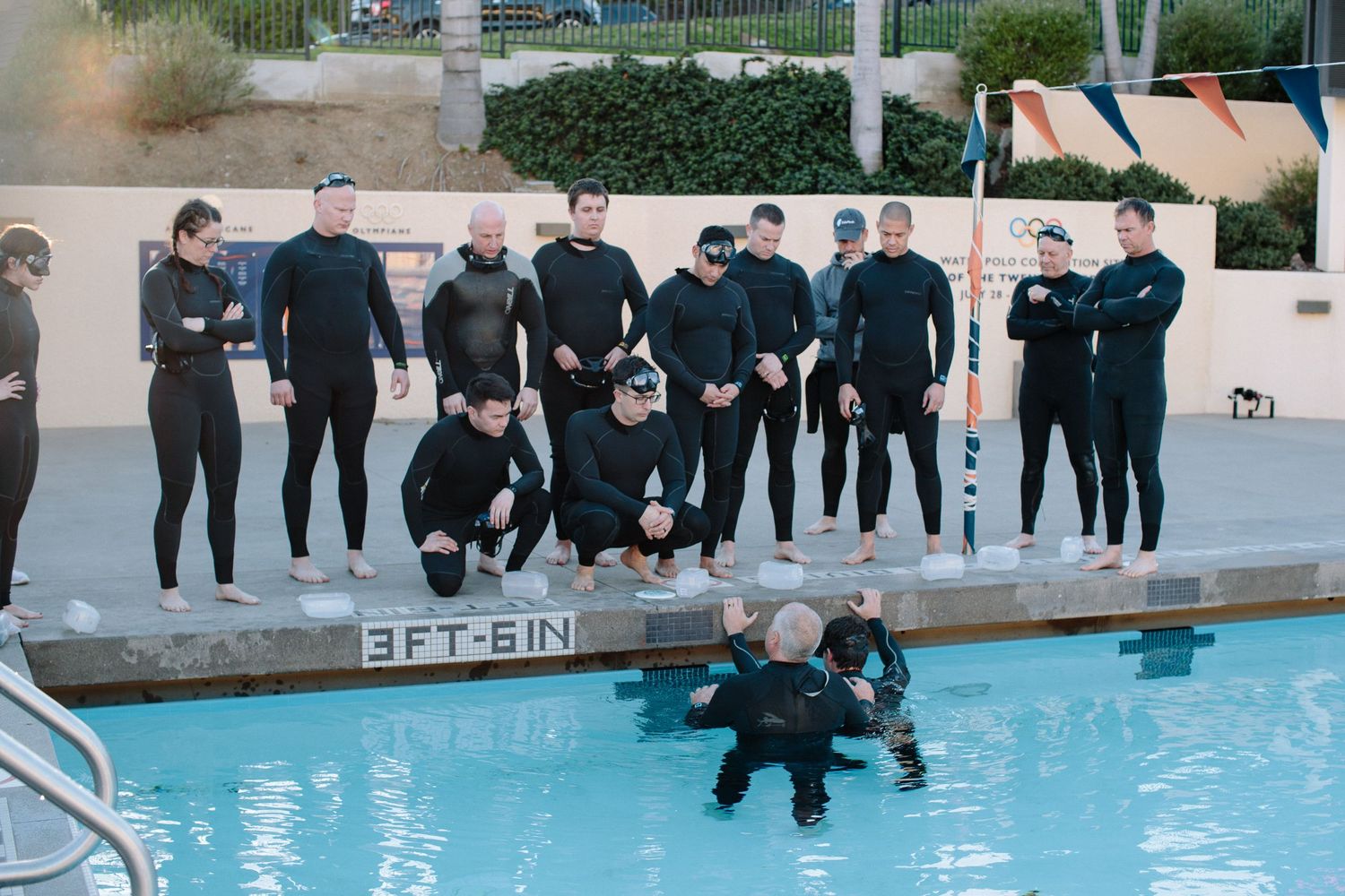 People lined up along the edge of a swimming pool prepare to enter the water.