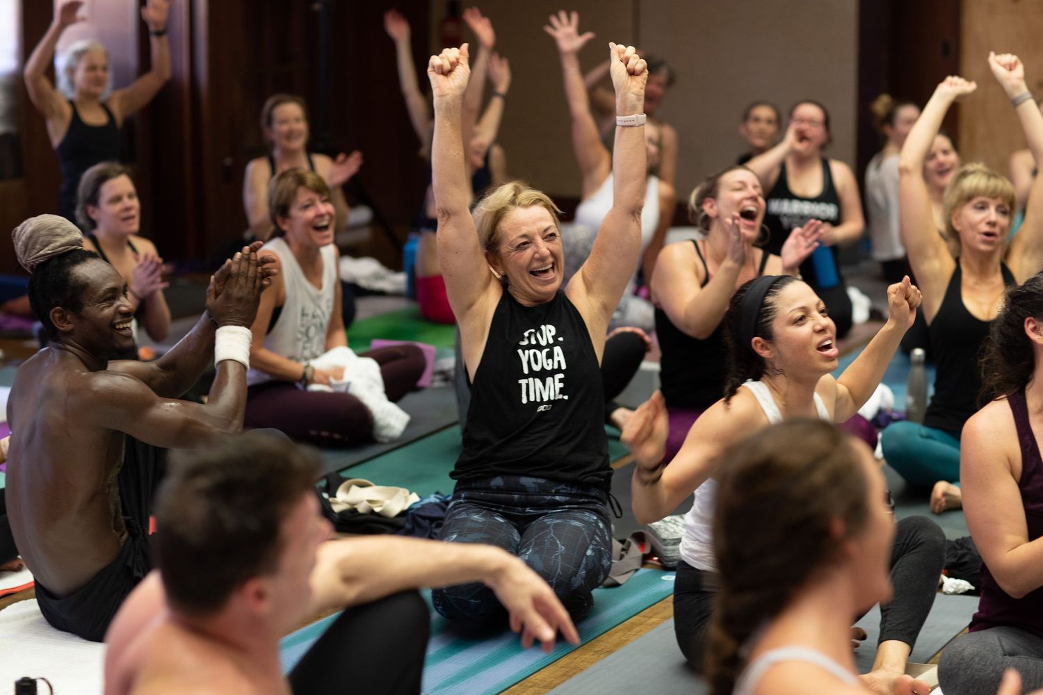 Enthusiastic group of yoga participants raising their arms during an energetic class session.