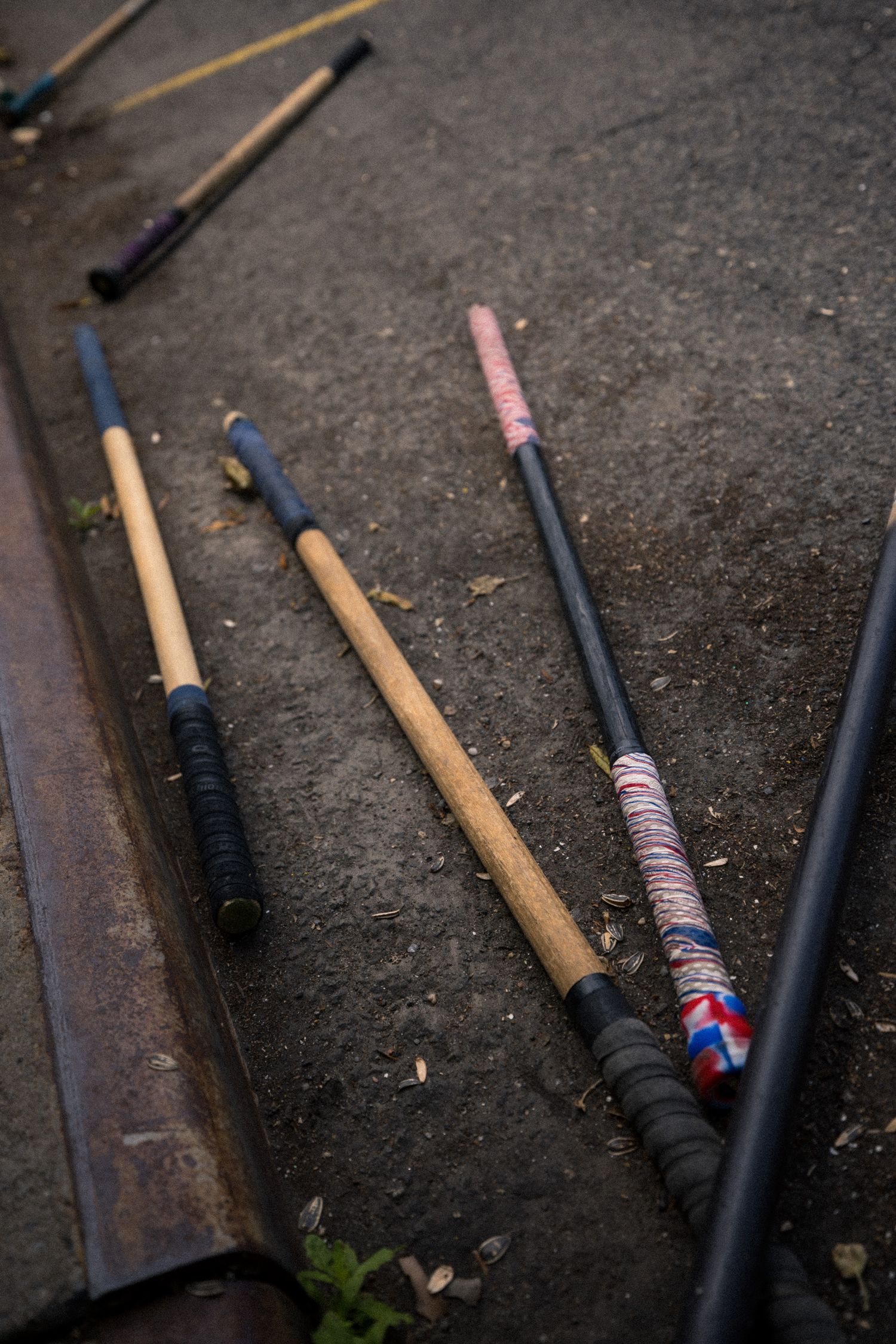 Several wooden bats and sticks lying on a concrete surface with colorful grip tape wrappings.