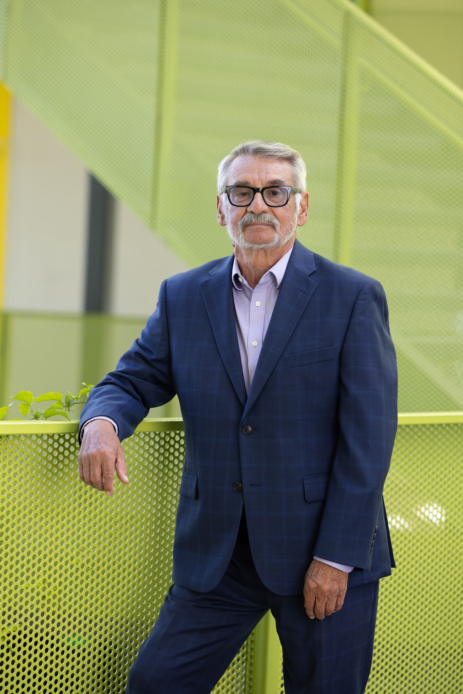 Executive portraits of someone in a navy suit posing against a modern lime green architectural backdrop.