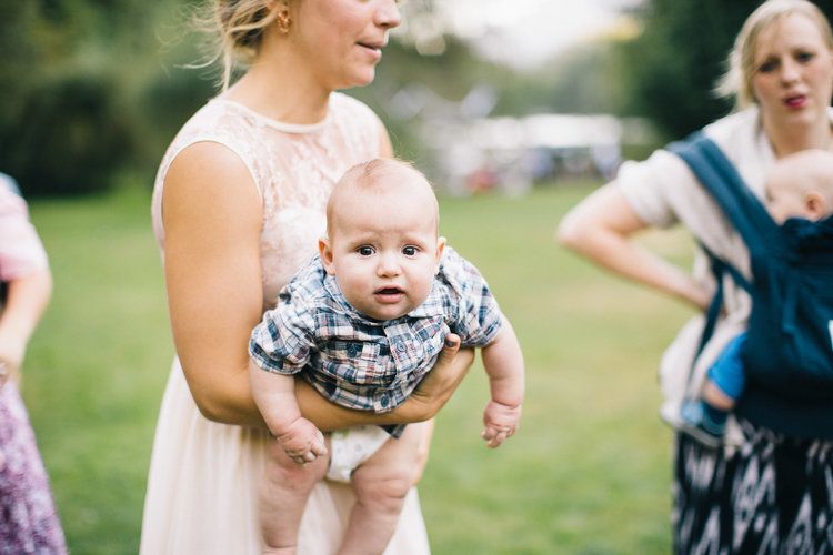 Woman in pink dress lifts a baby wearing plaid outdoors in a park.