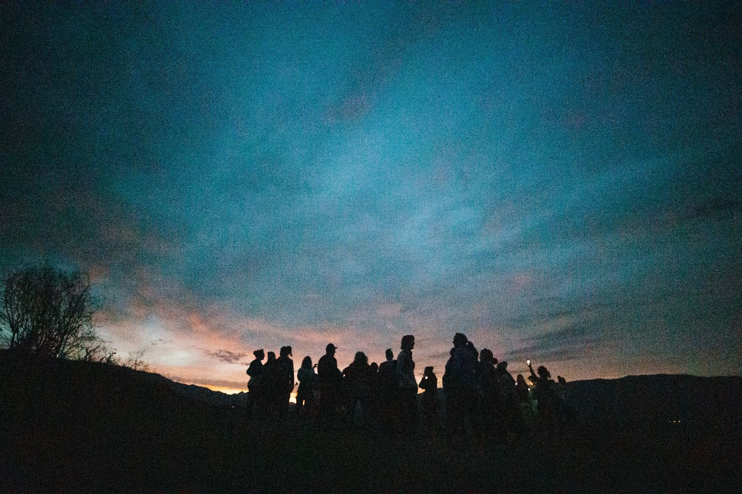 Silhouettes of people standing against a blue and purple sunset sky.