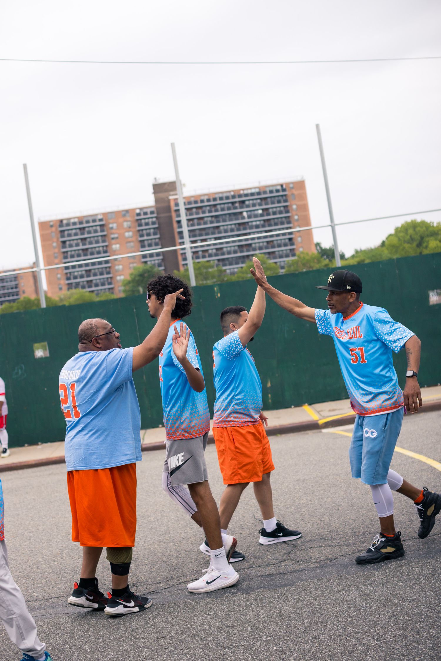 Group of players in blue jerseys celebrating with high fives on outdoor court.