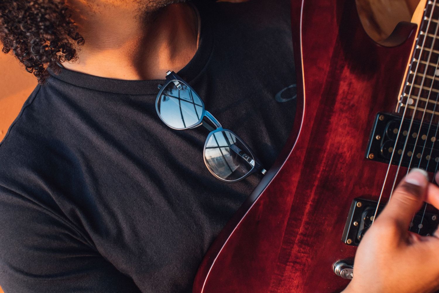 Close-up of Oakley sunglasses hanging on black t-shirt next to red electric guitar for Oakley in store POP, website and otherwise