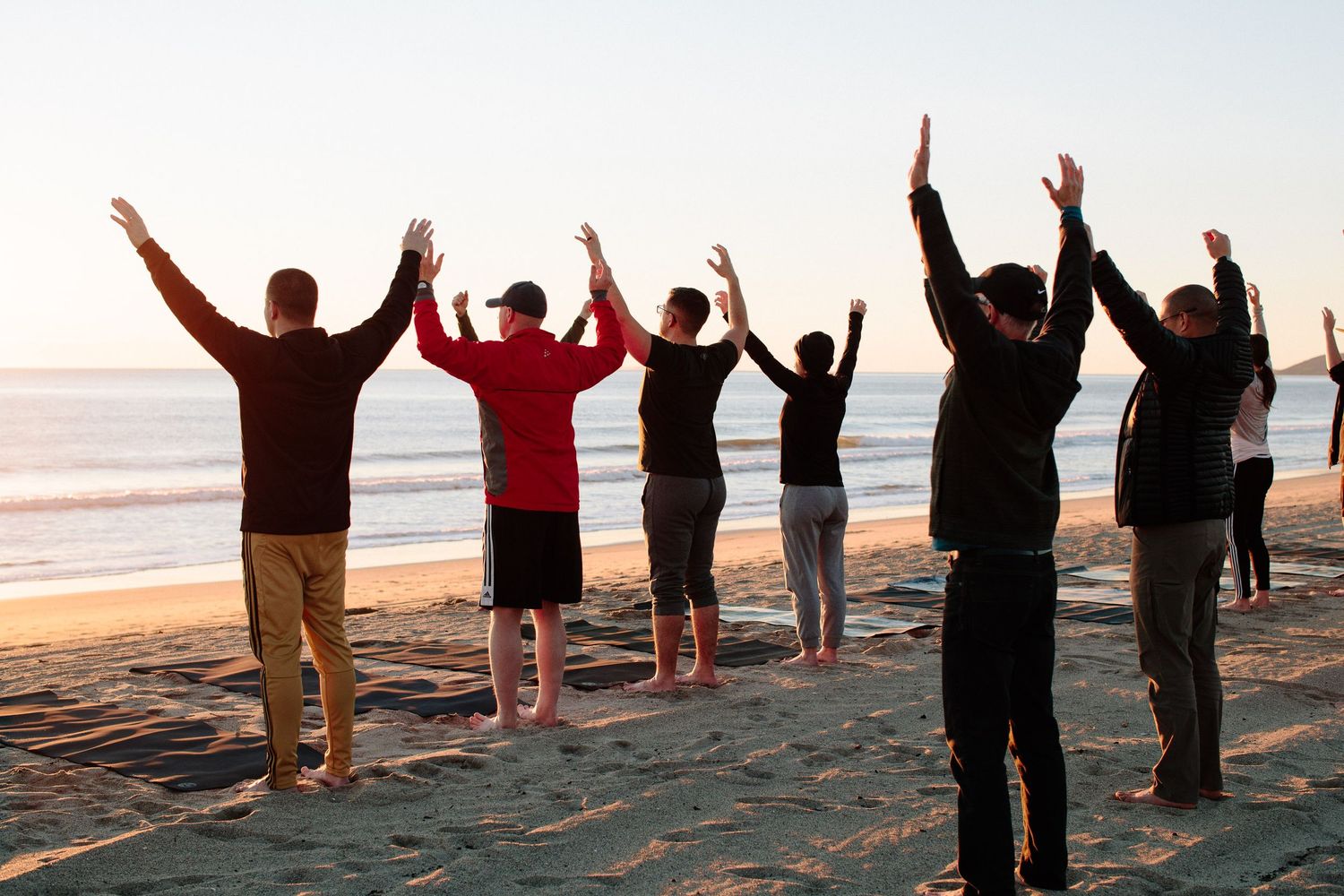 Silhouetted figures raise their arms in celebration against a sunset beach backdrop.