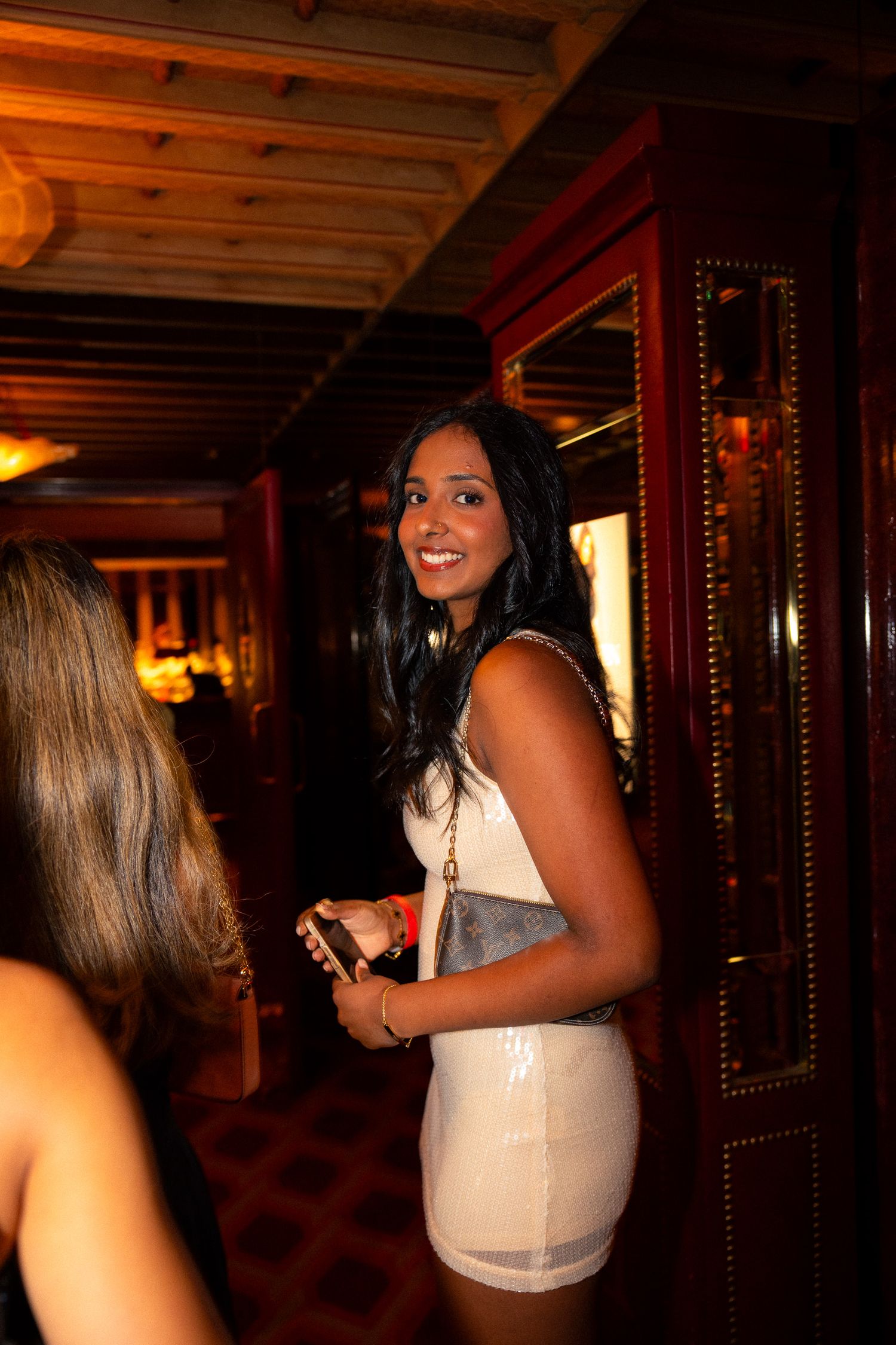 Woman in a beige dress smiles while standing in an elegant venue hallway.