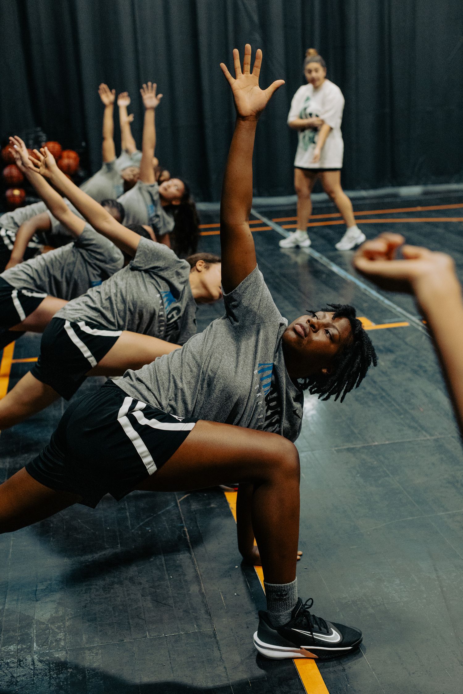 Athletes perform stretching exercises on indoor basketball court during team practice.