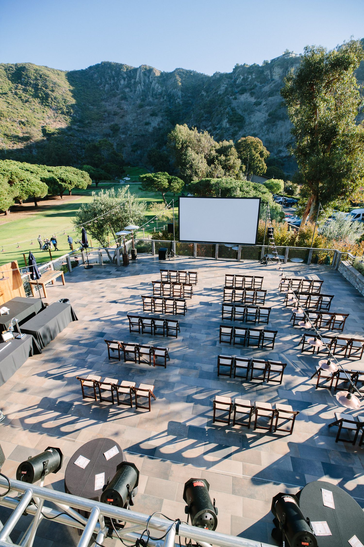 Outdoor wedding ceremony setup with black chairs arranged in rows on a stone patio surrounded by mountain scenery.