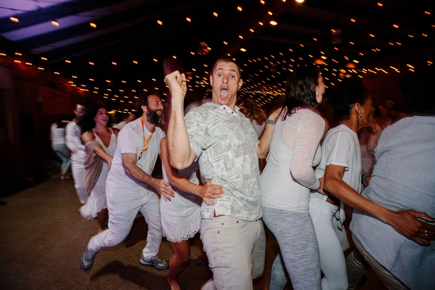 A lively dance party scene with people in white outfits dancing under string lights.