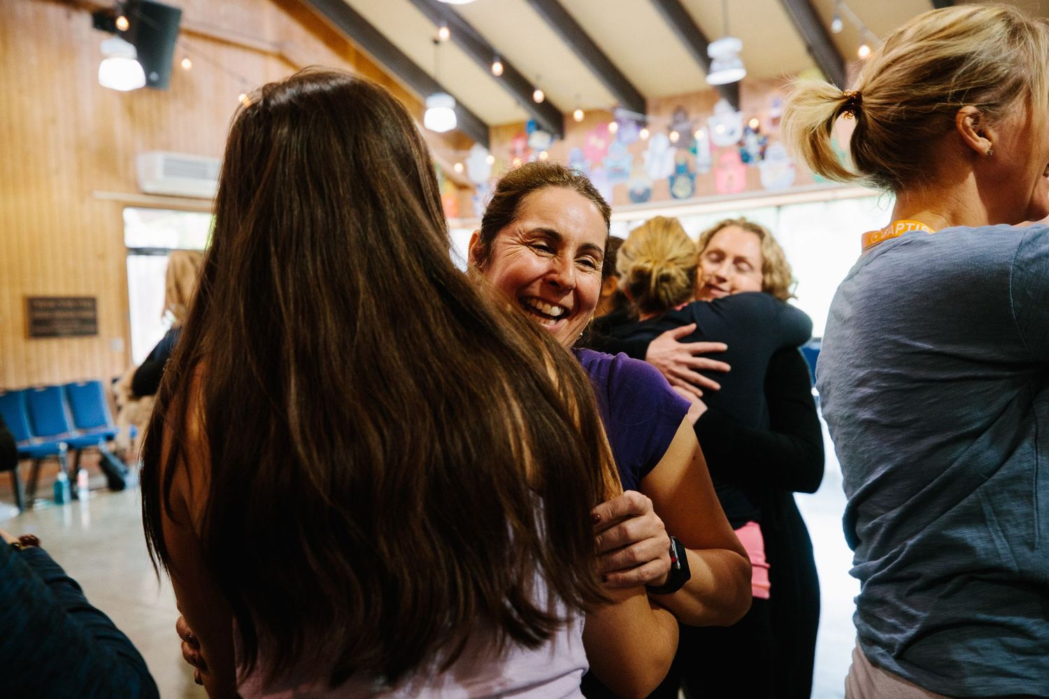 Crowd of people gathered in an indoor venue with wooden paneled walls and bright lighting.