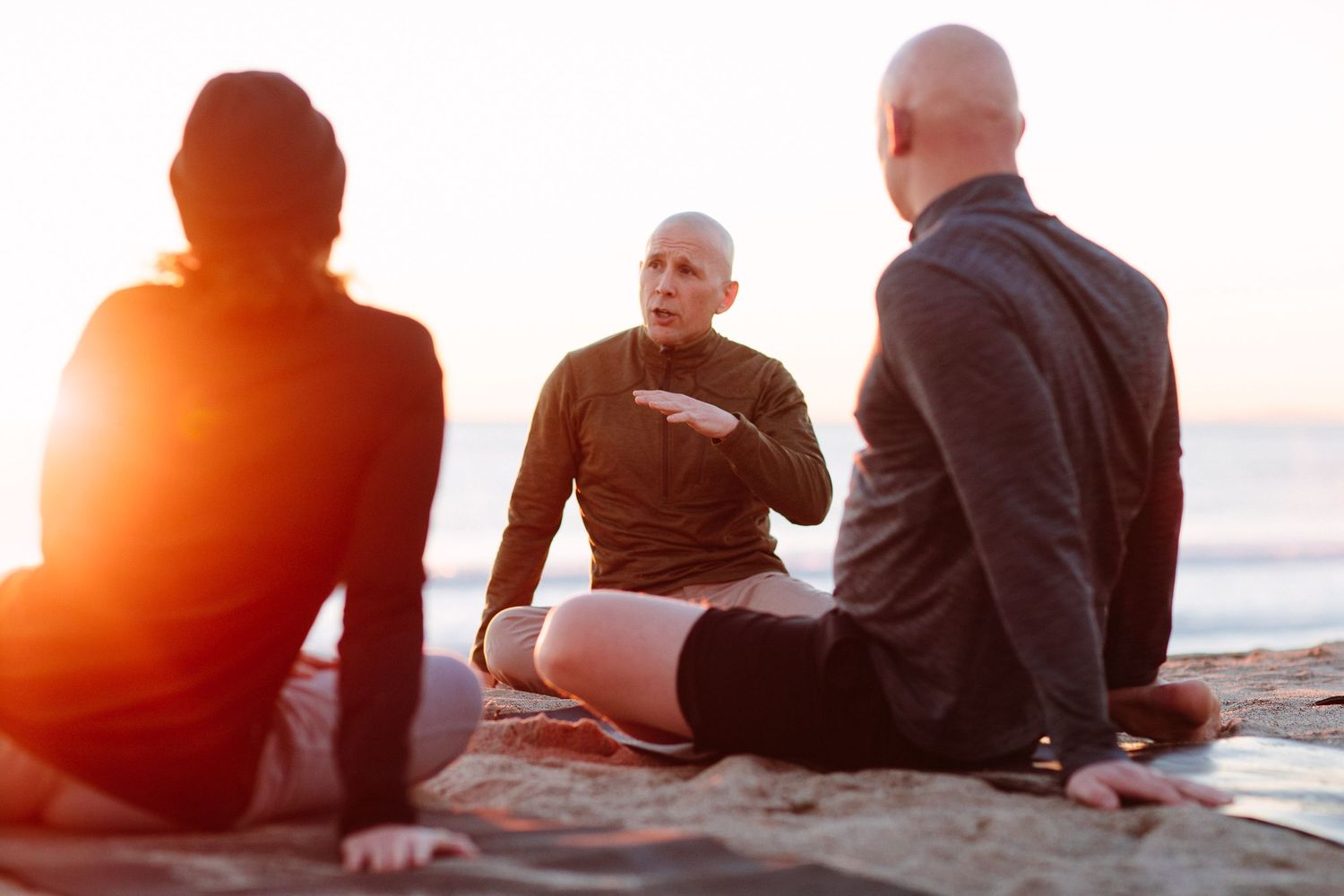 People relaxing and sitting together on beach during golden hour sunset.