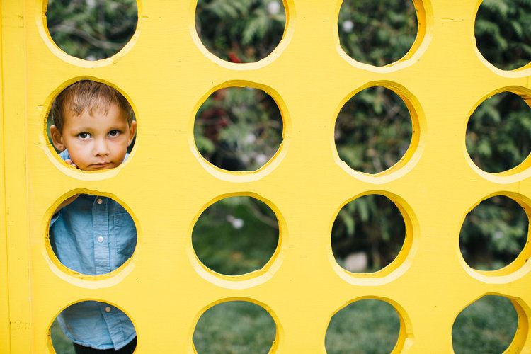 Child peeking playfully through yellow connect-four style game board.
