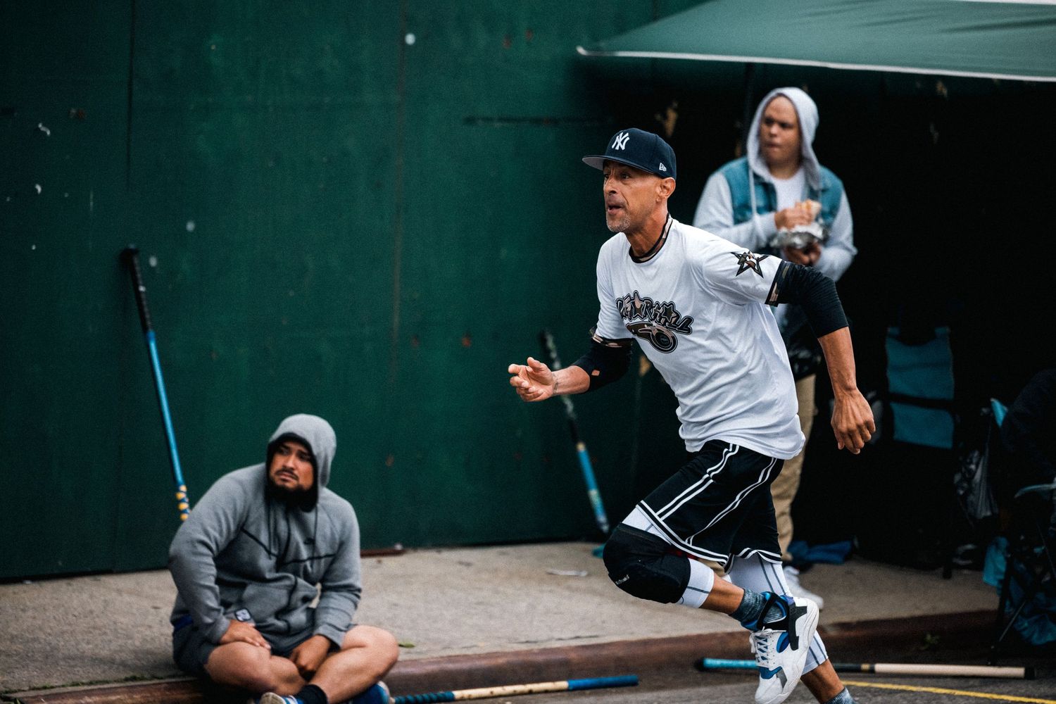 Players practicing basketball moves on an outdoor court with dark green walls.