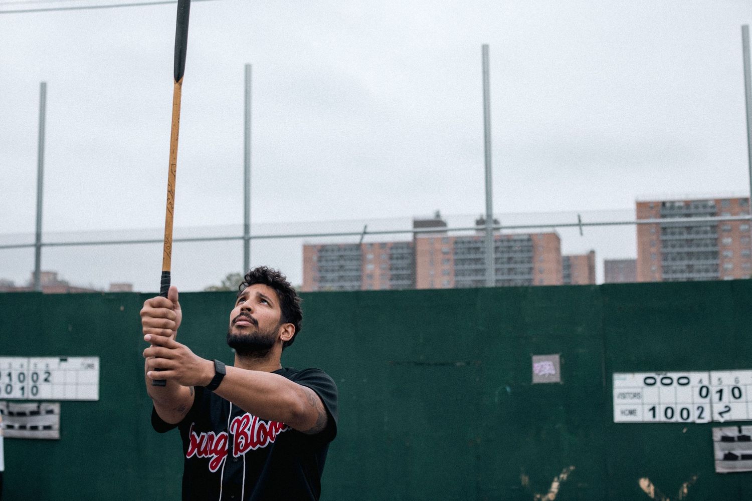 Someone practicing their baseball swing at a batting cage with apartment buildings visible in the background.