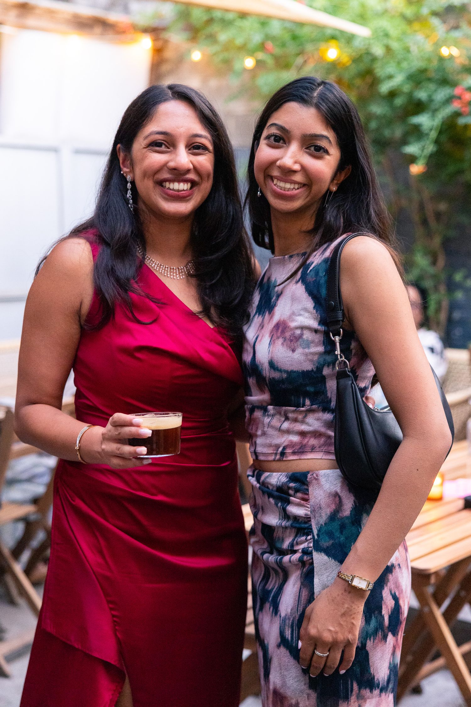 Friends in formal attire smiling and posing together at outdoor party with string lights.
