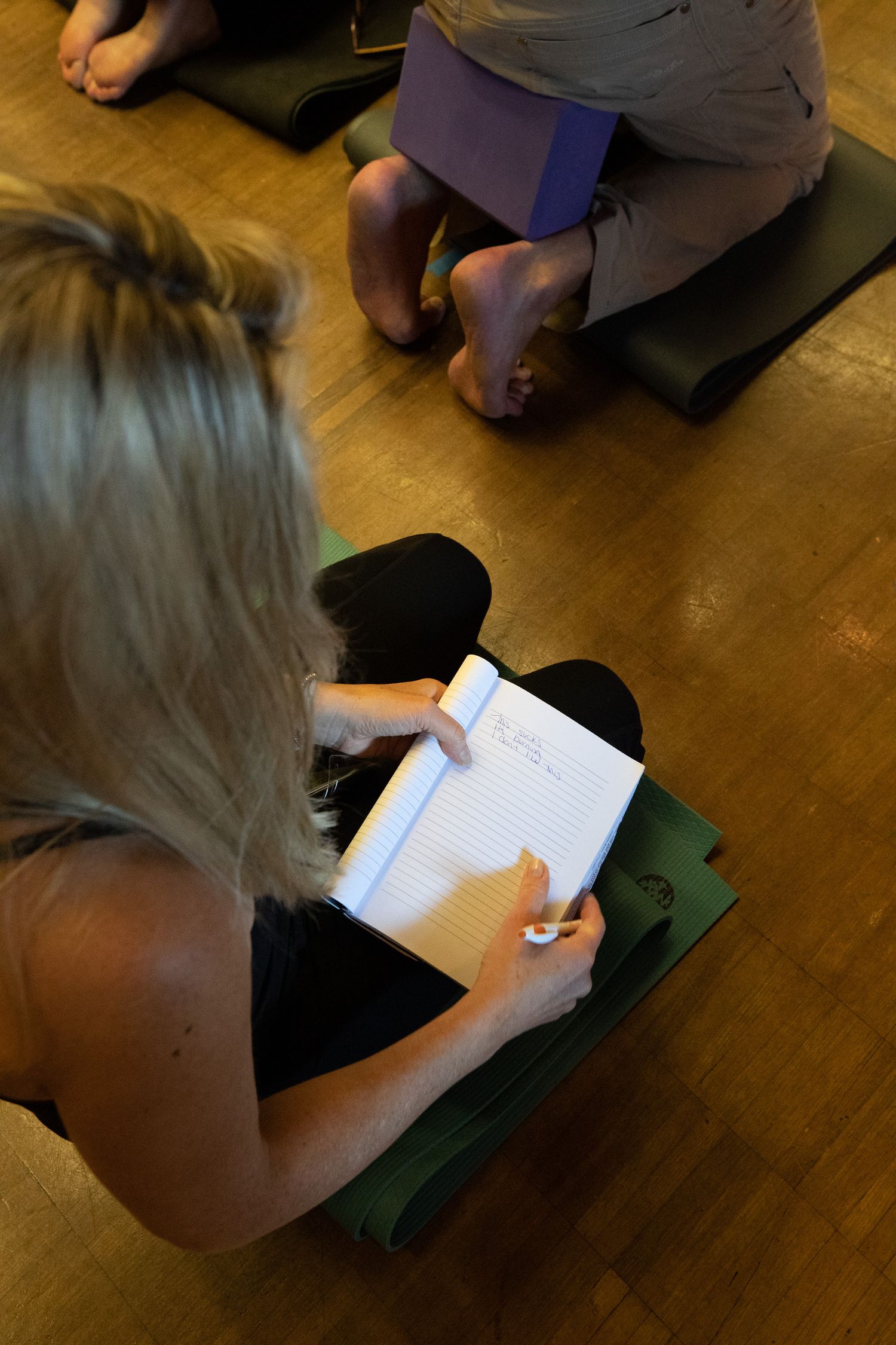 Person taking notes while sitting on a yoga mat during a wellness session.