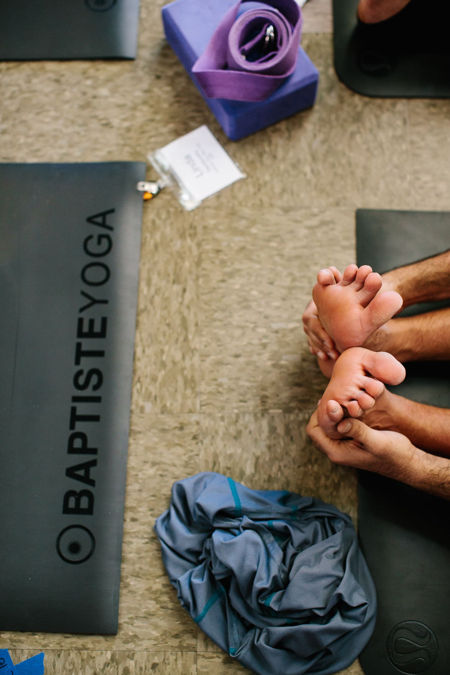 Close-up of clasped hands resting on grey yoga mats during meditation.