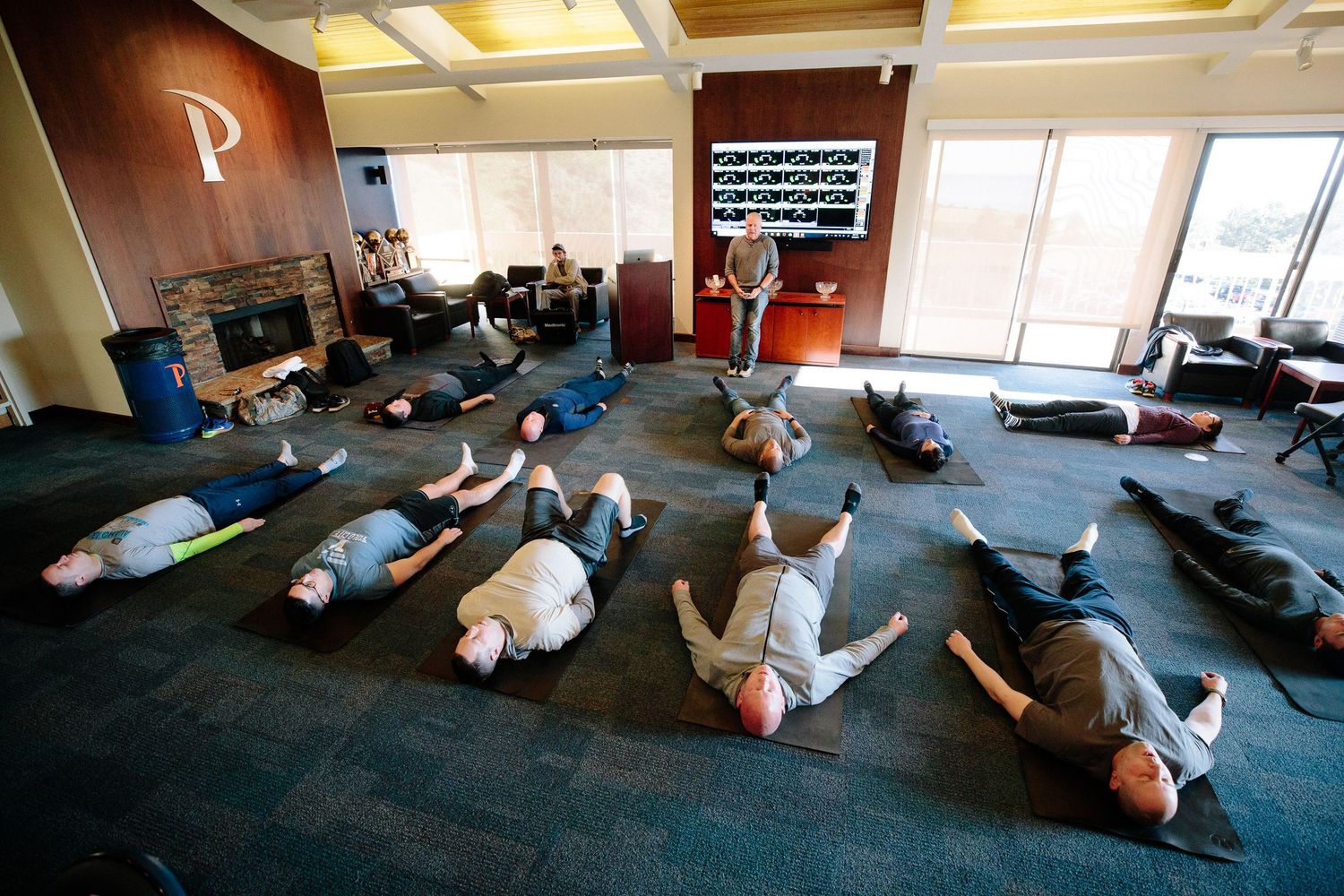 Group fitness session with participants lying on floor doing exercises in modern office space.