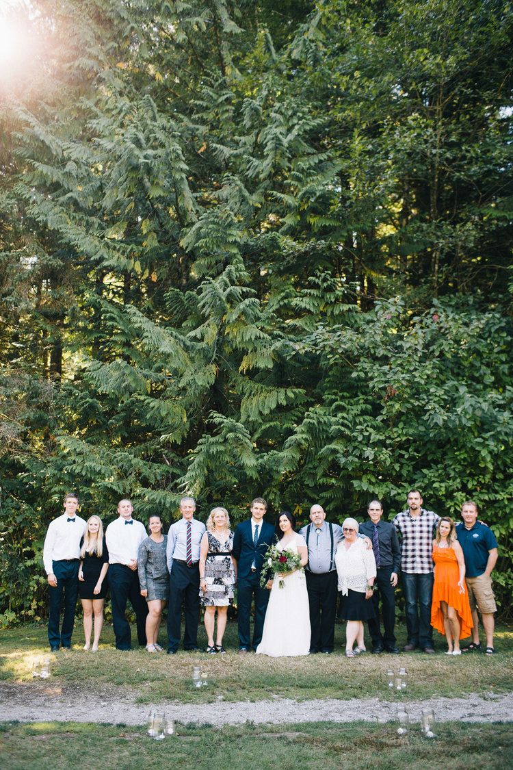 Wedding party group photo in front of lush green forest backdrop.