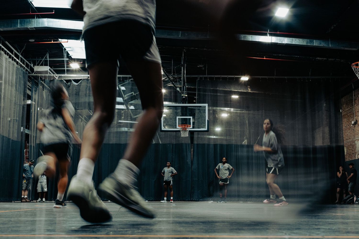 Players in athletic wear compete during an evening basketball game in a dimly lit indoor gymnasium.