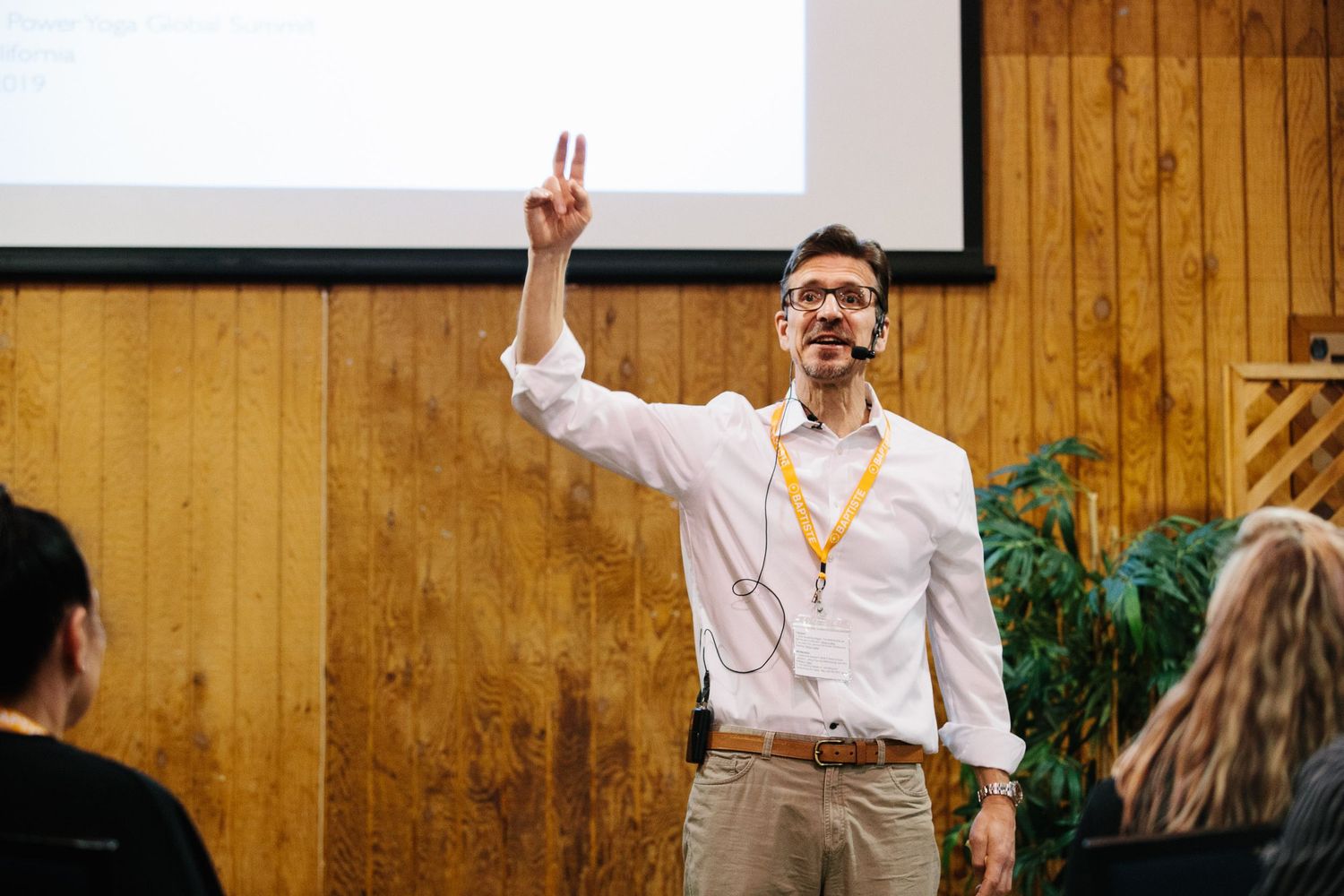 Presenter gesturing energetically while speaking at a workshop with wooden wall background.