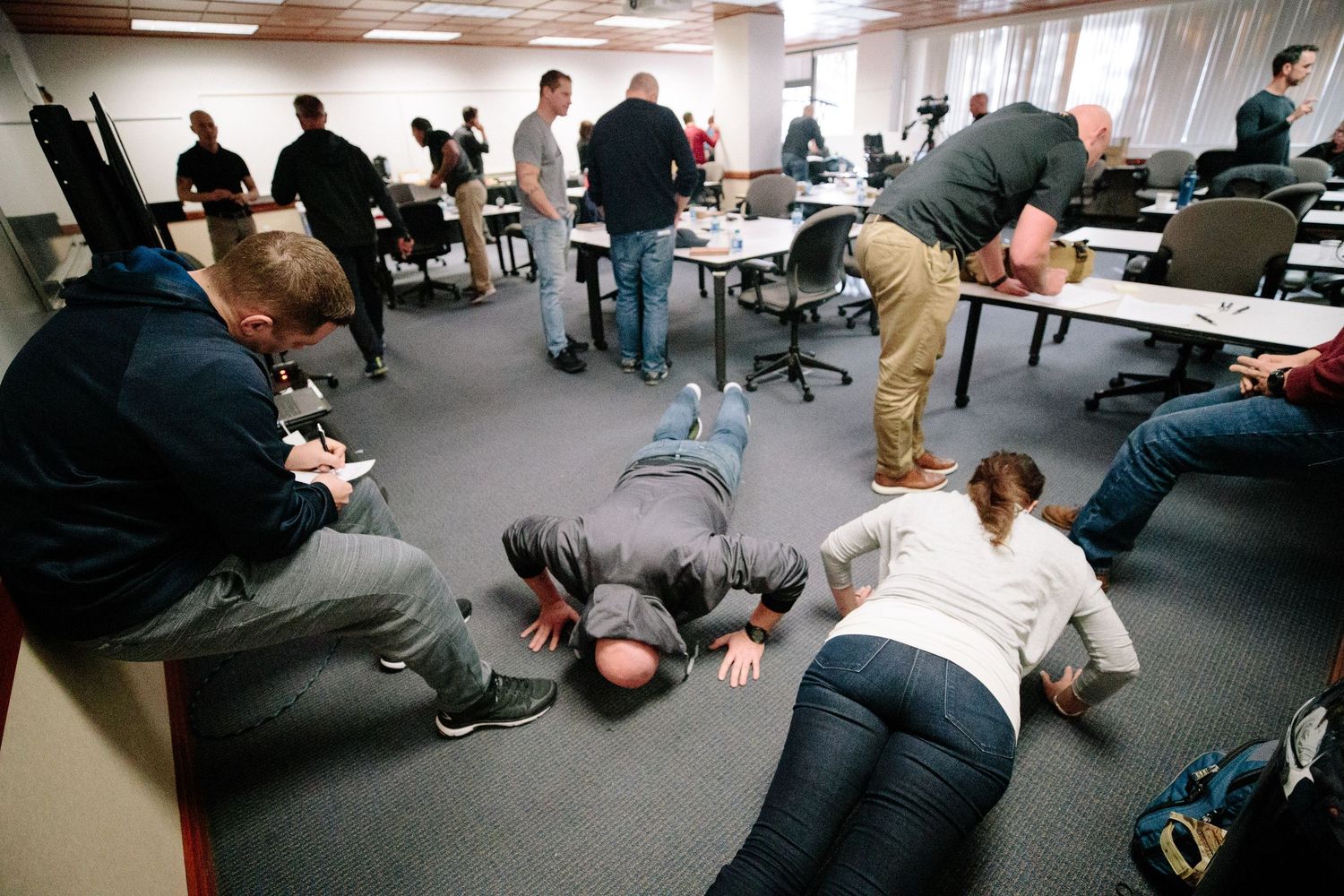 People participate in floor exercises in an indoor office or conference room setting.