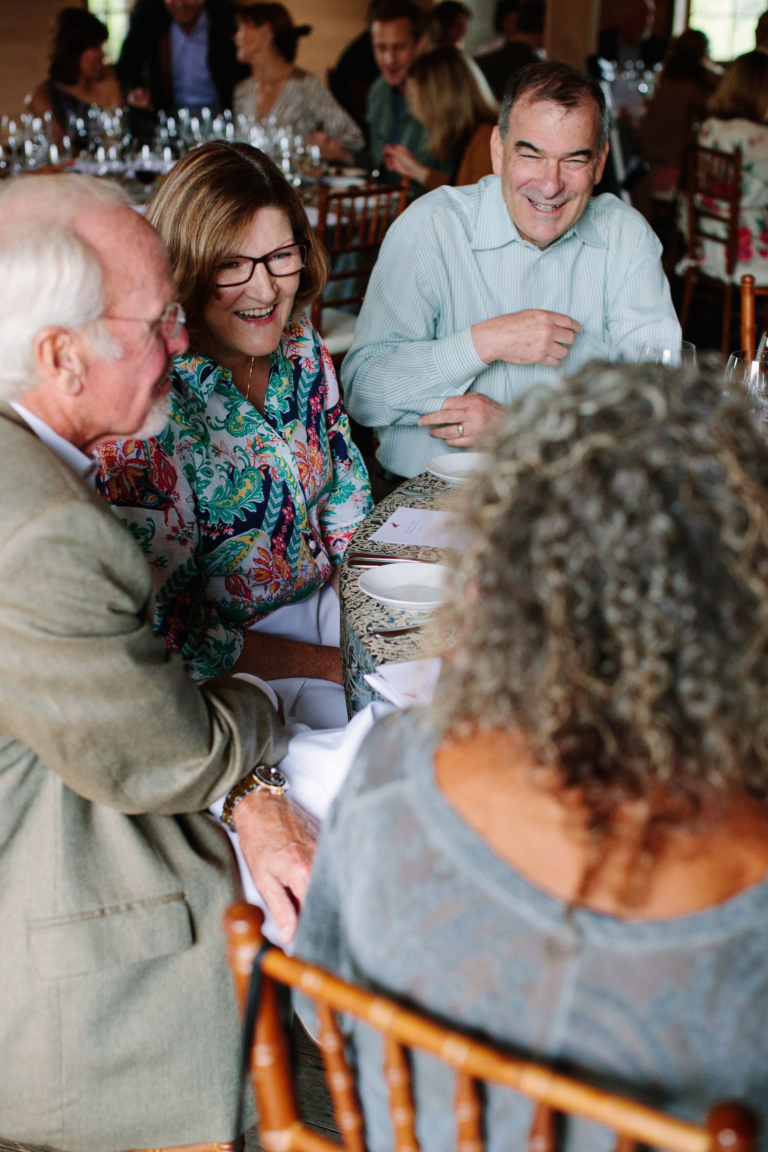 A group of people laugh and socialize around a formal dining table at an event.