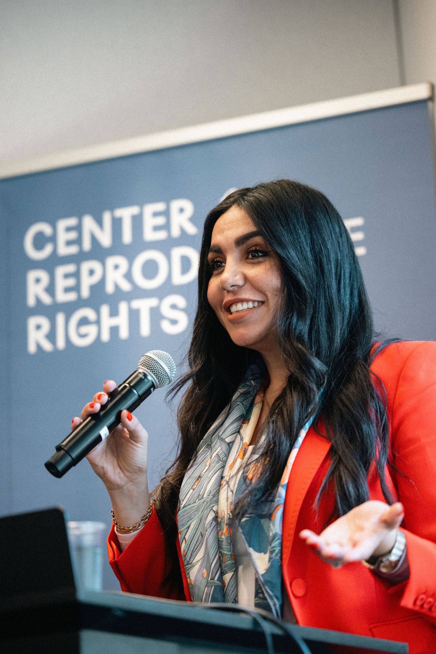 A speaker in a bright red blazer holds a microphone while presenting at the Center for Reproductive Rights.