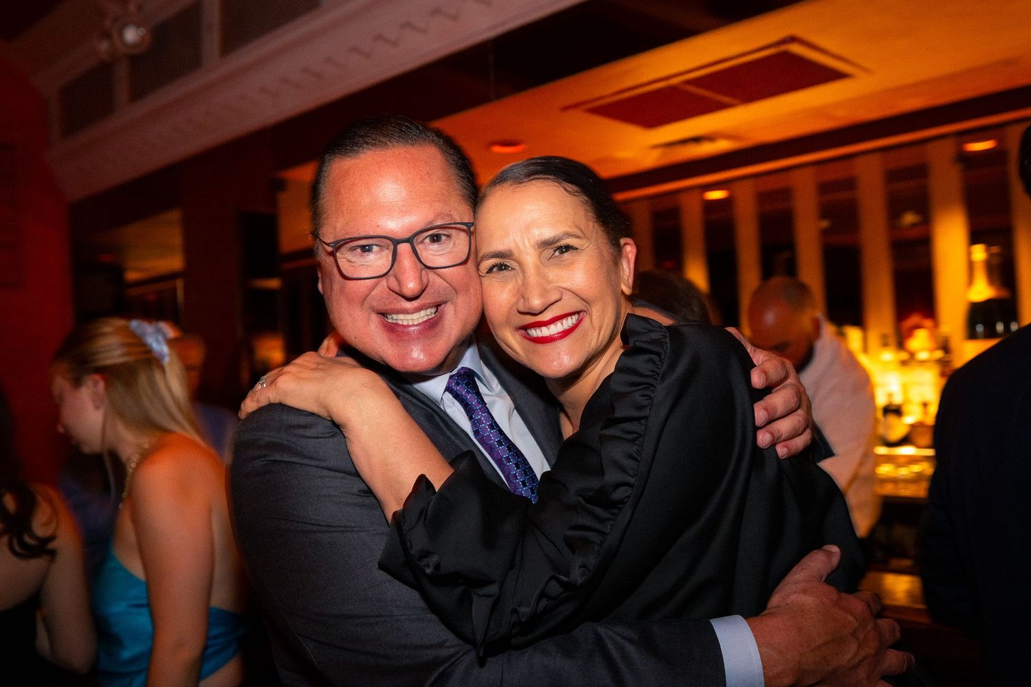 Two attendees share a warm embrace at an indoor social function.