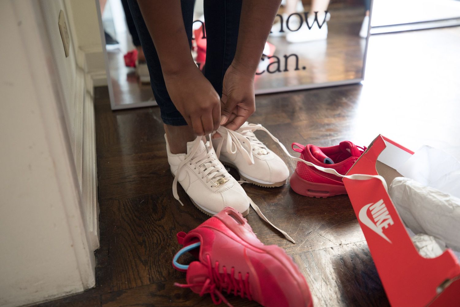 Woman trying on red and white Nike running shoes while sitting.