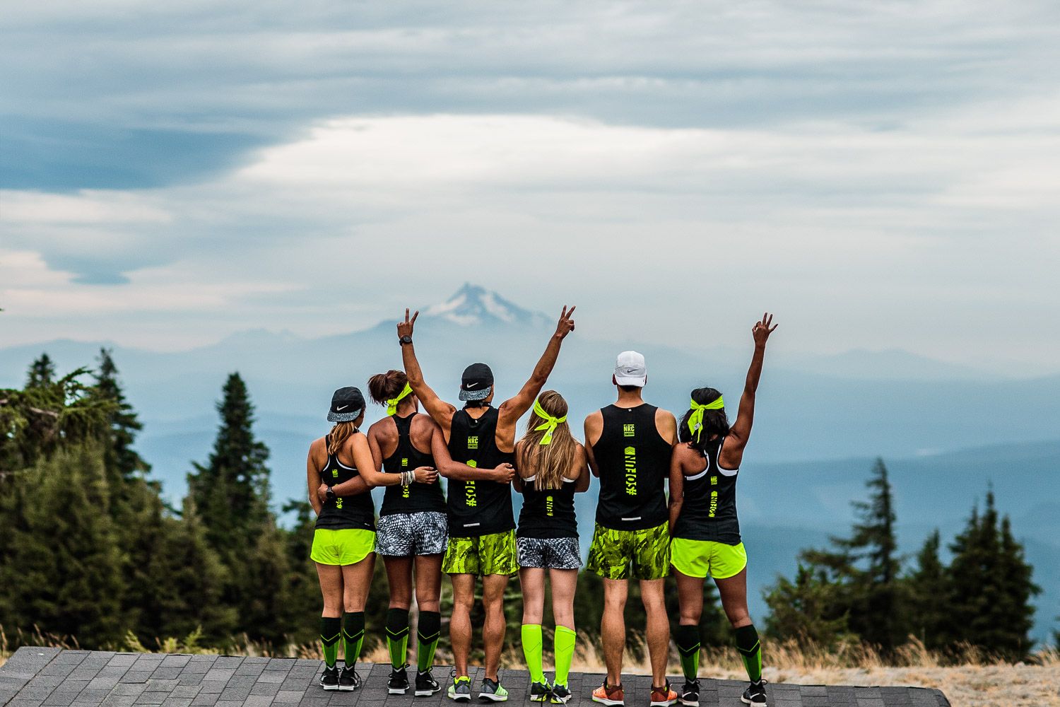 Group of runners celebrating on a scenic mountain summit against a cloudy sky.