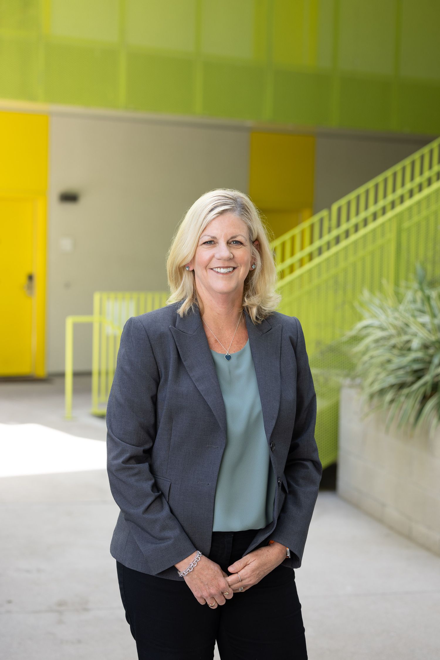 Corporate portraits of someone in dark blazer and teal top against a bright yellow and green background.