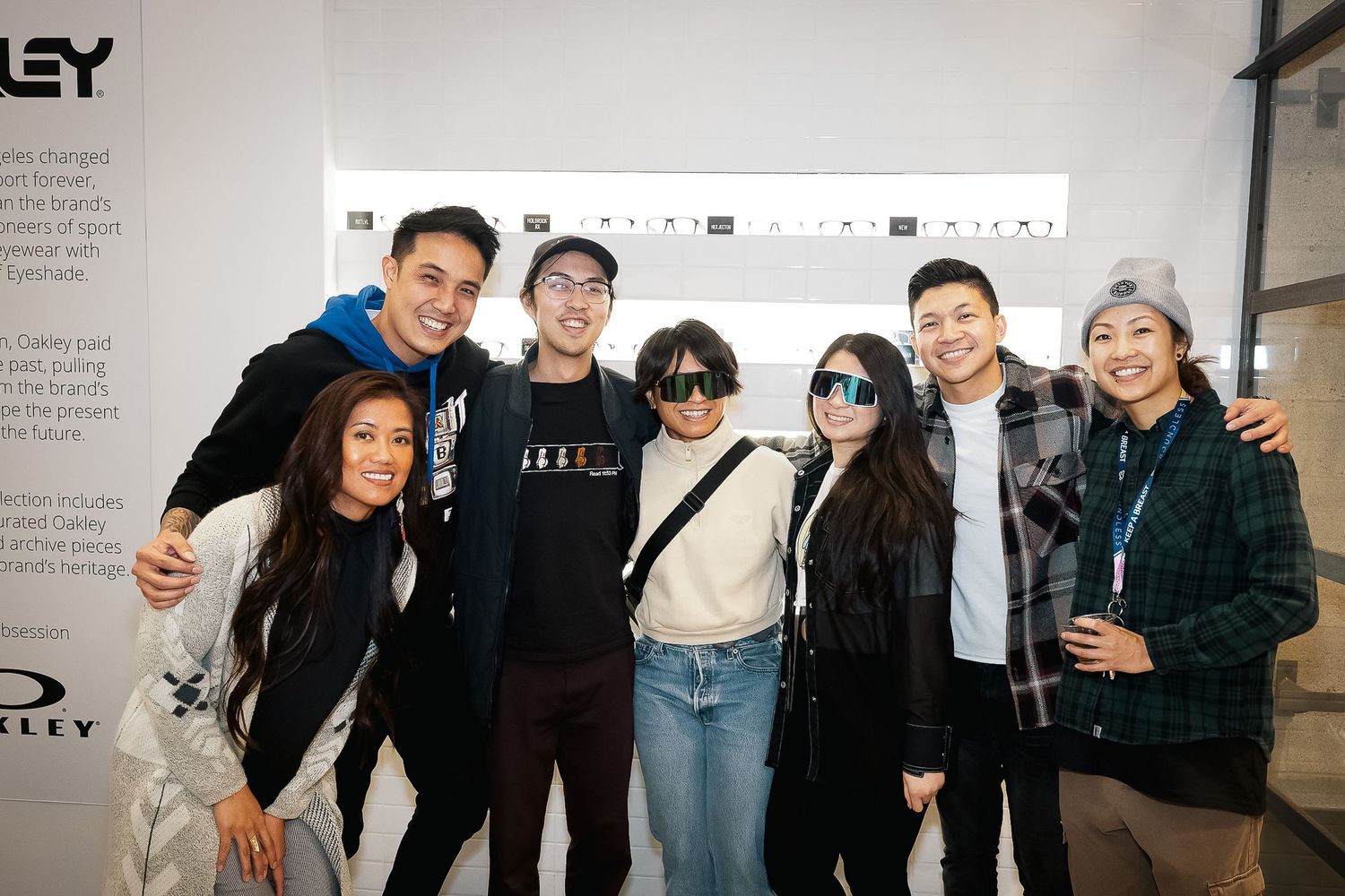 A group of friends pose together smiling in a bright indoor space with a white wall behind them.