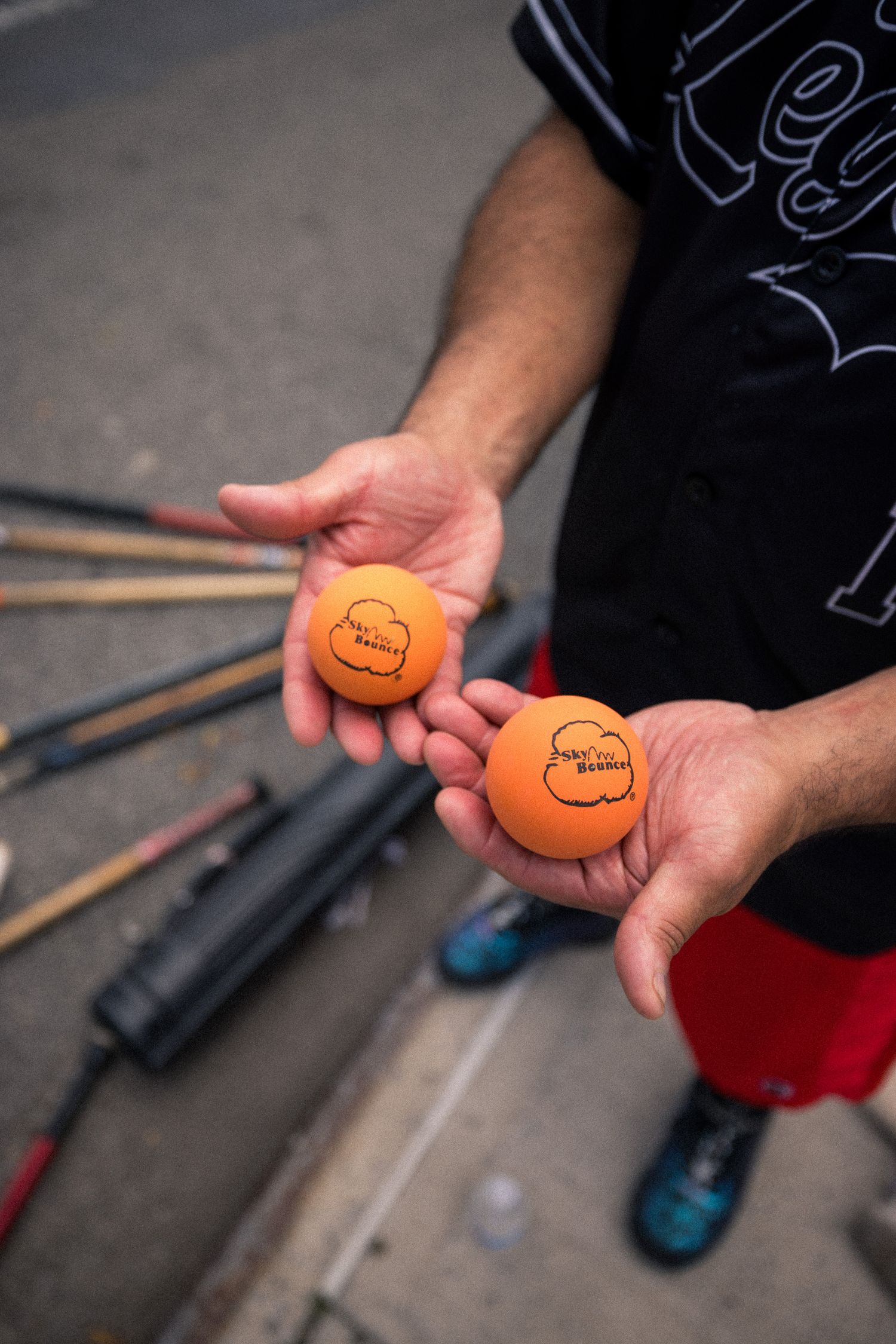 Two orange street hockey balls held in hands with wooden sticks visible in the background.