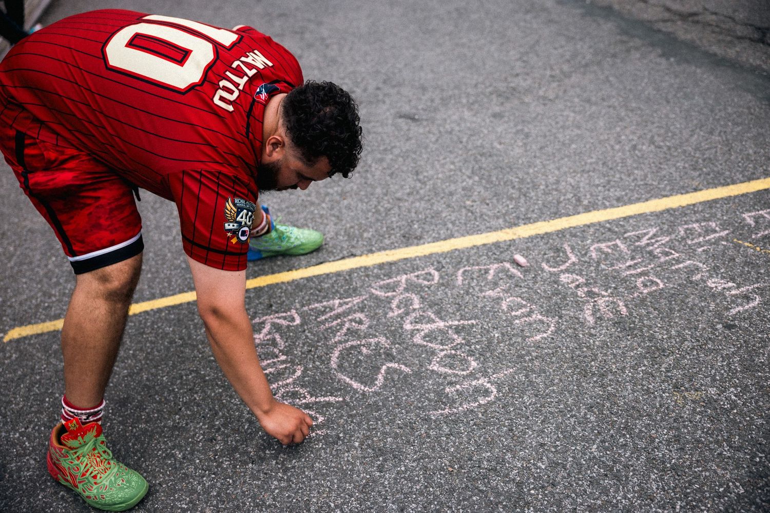 Person in red shorts demonstrates low crouching position during stickball game on concrete court.
