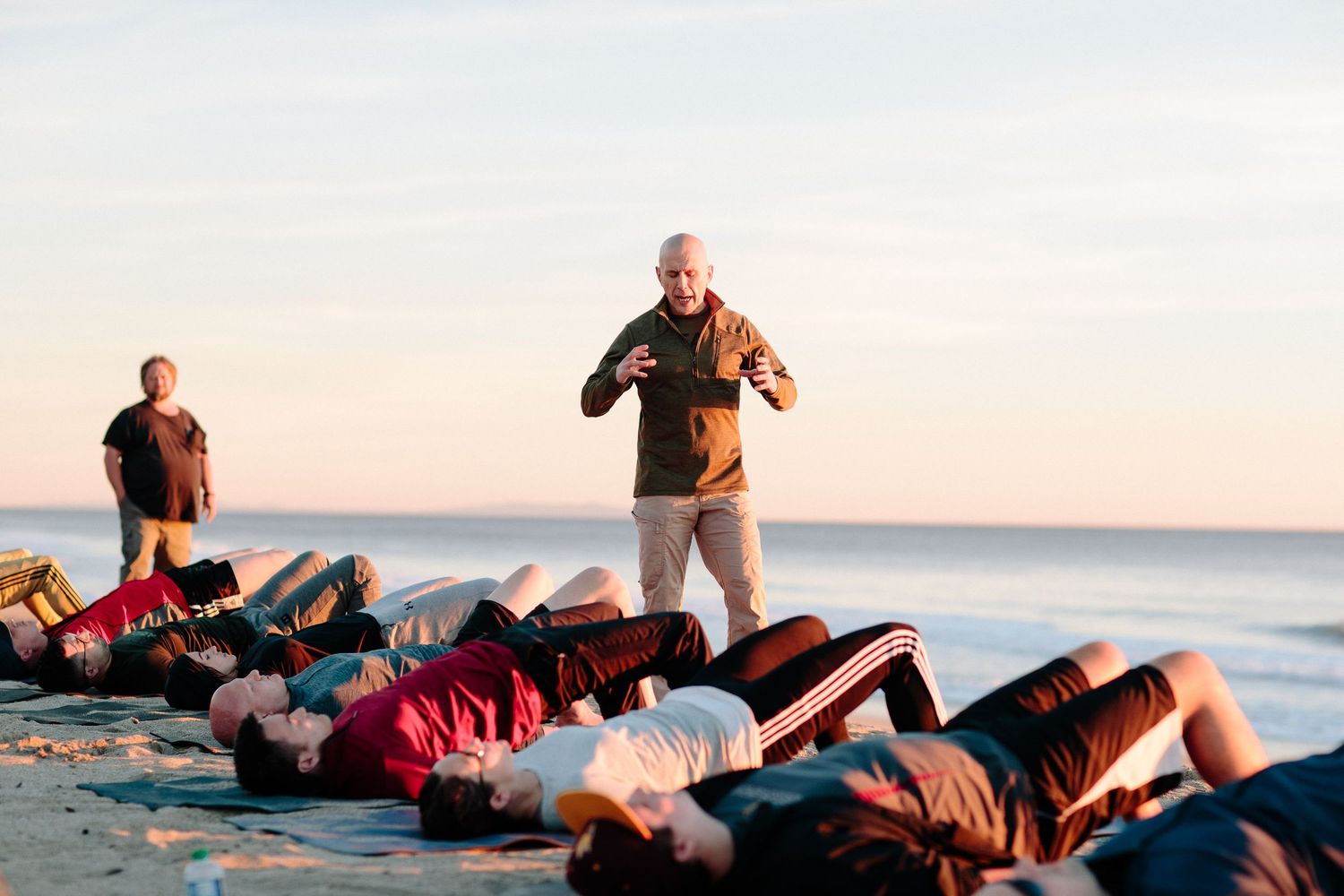 Group practicing physical exercises outdoors at sunset by the ocean.
