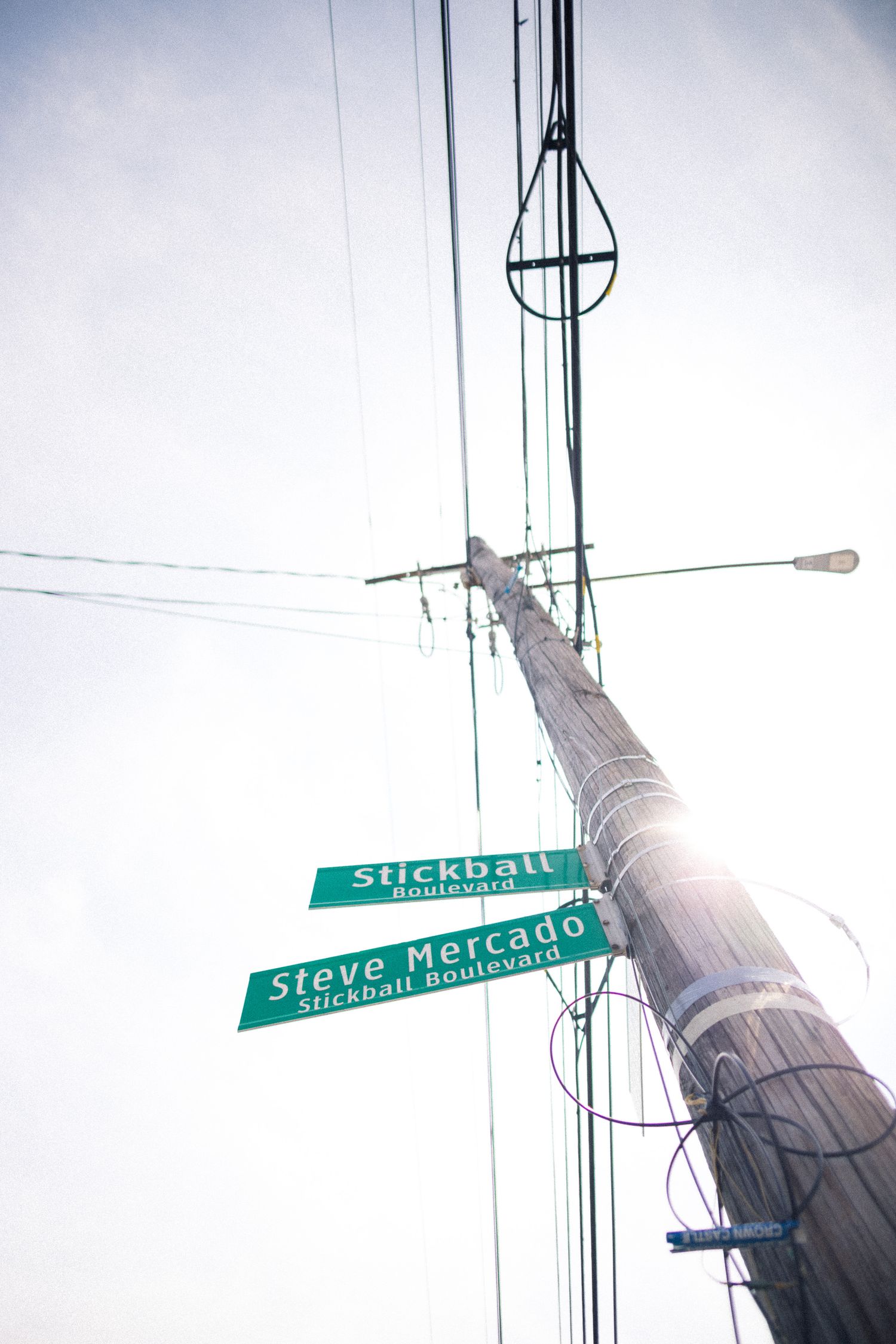 Low angle view of a street sign intersection showing Stickball Street and Steve Mercado Street against utility pole and sky.