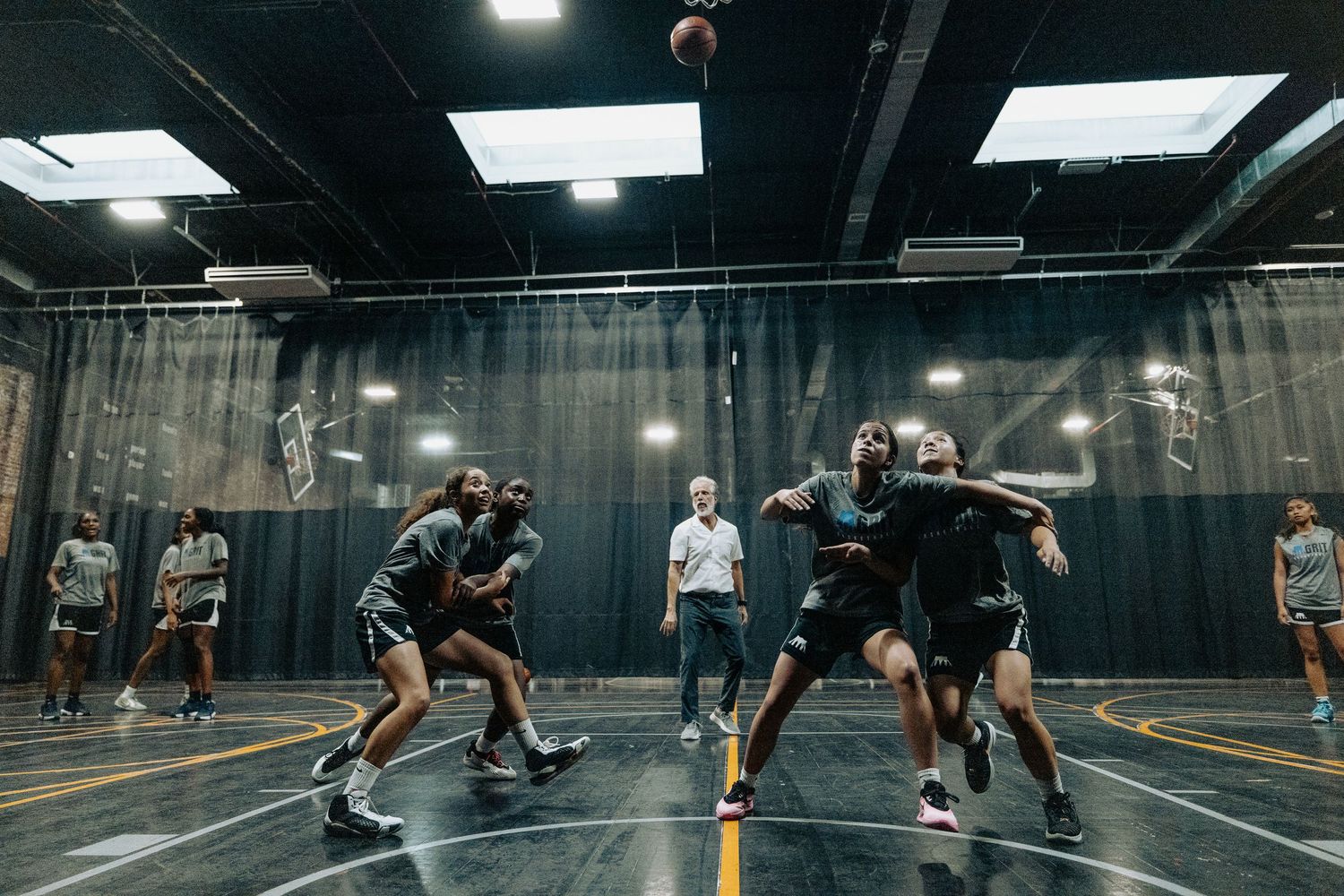 Basketball players engaged in a practice scrimmage on indoor court.
