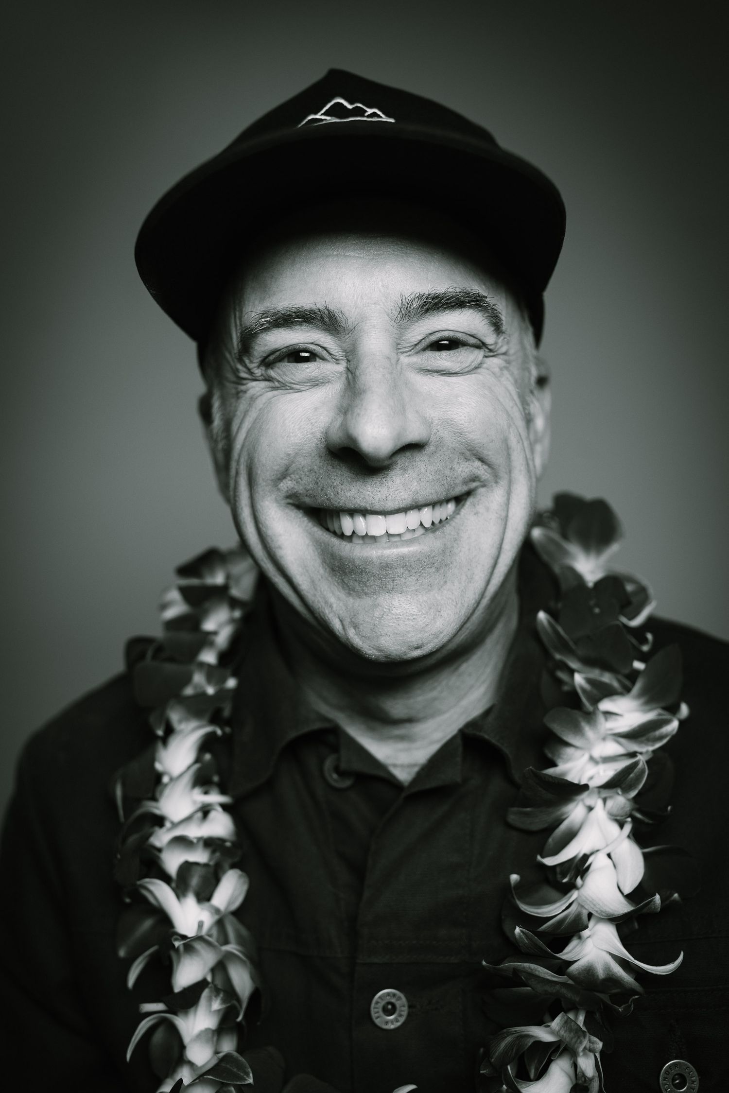 Cheerful portrait with baseball cap and Hawaiian lei against dark background.