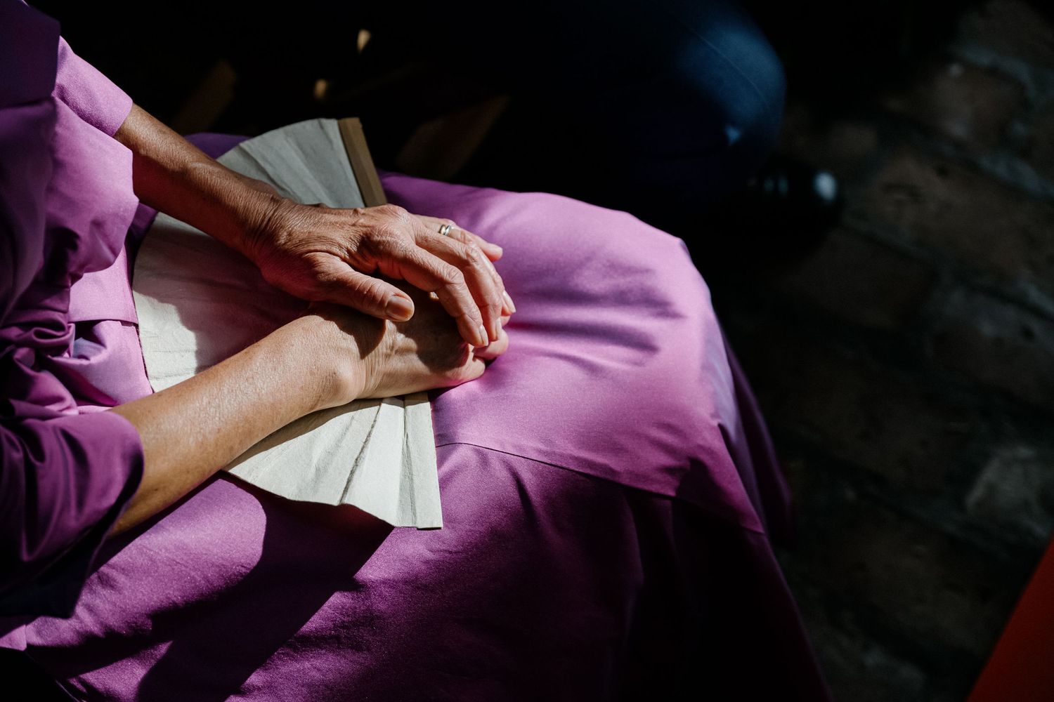 Hands rest gently holding a book over a vibrant purple dress fabric in dramatic lighting.