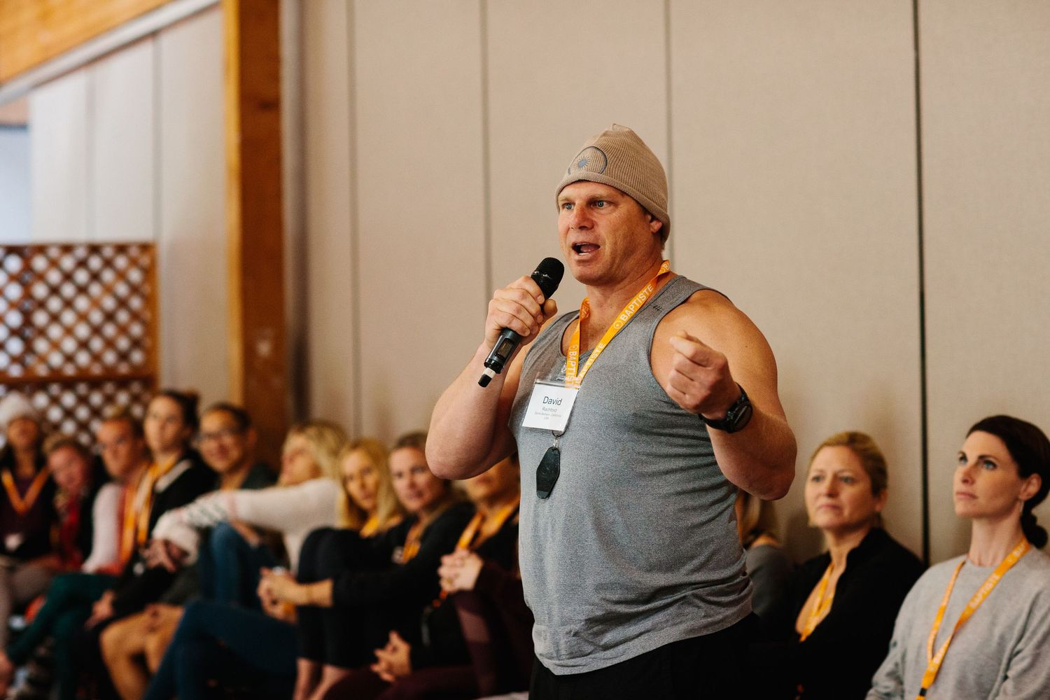 A person speaks into a microphone while gesturing during an indoor presentation.