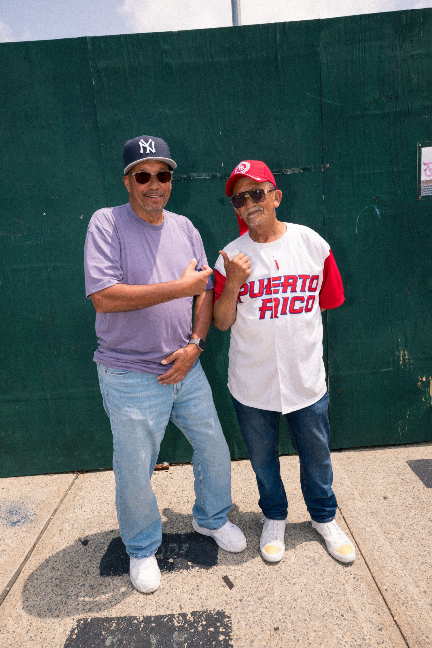 Three men lean against a green wall wearing casual attire with one wearing a Puerto Rico shirt.