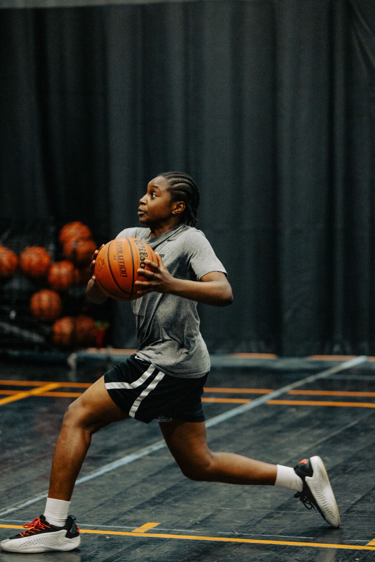 Basketball player in gray shirt and shorts practices dribbling moves on indoor court.