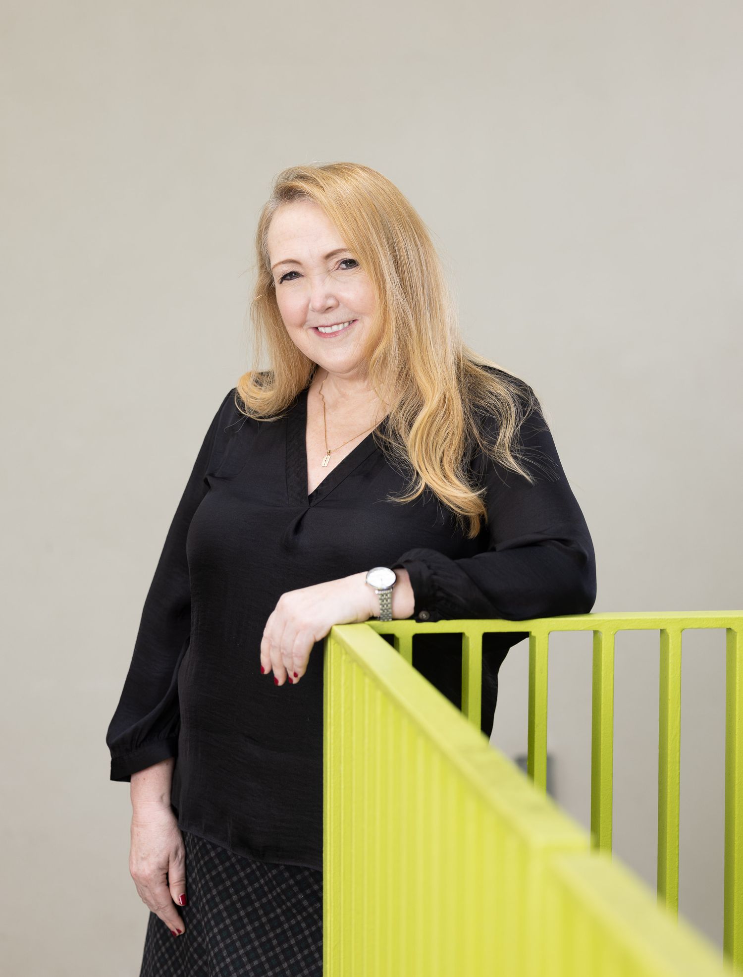Professional headshots of someone in business attire posing by a bright yellow railing.