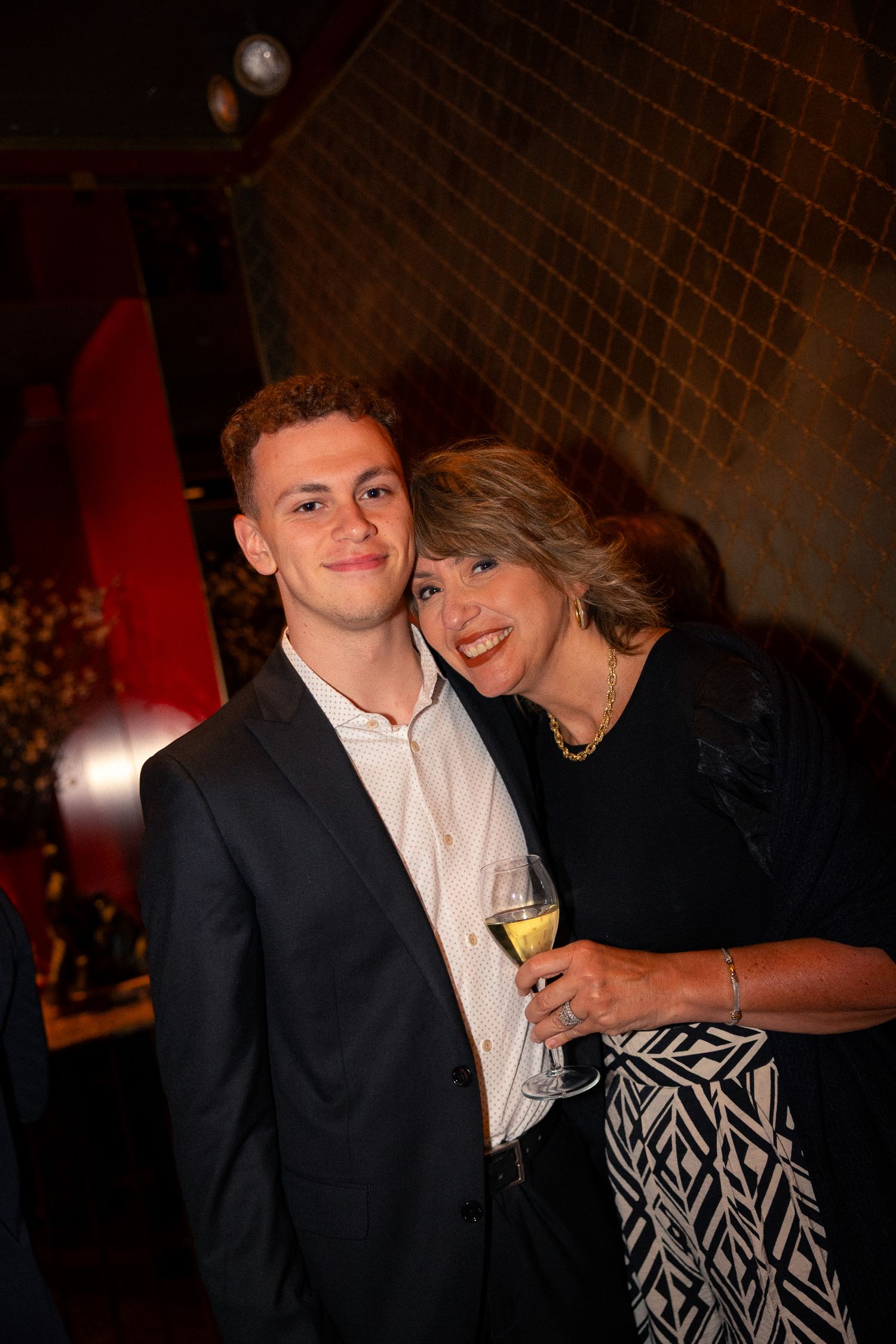 Two people pose together at an evening social event with wine glasses.